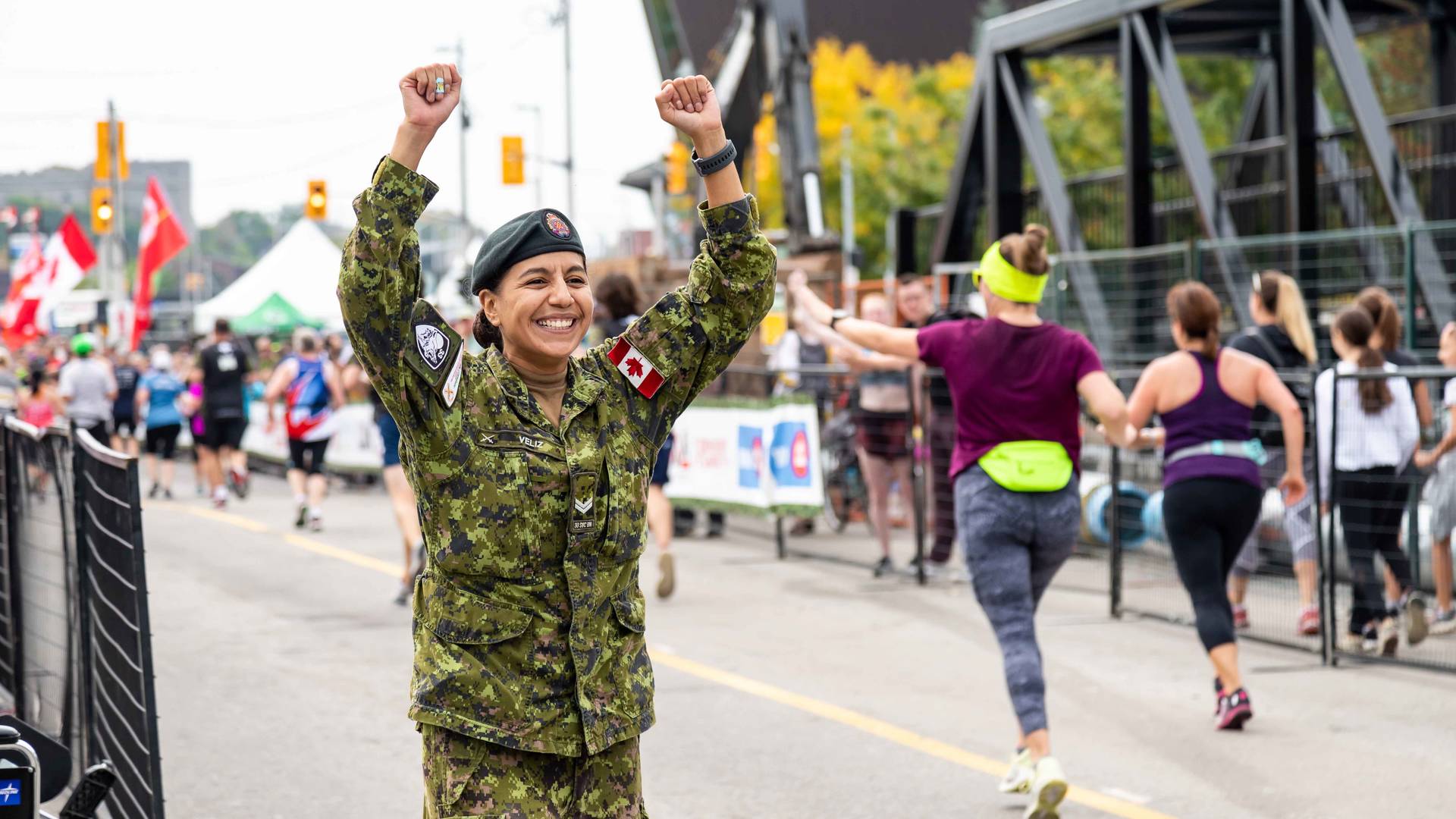 Member of the Canadian Armed Forces throwing her hands up and cheering along runners at the Canada Army Run