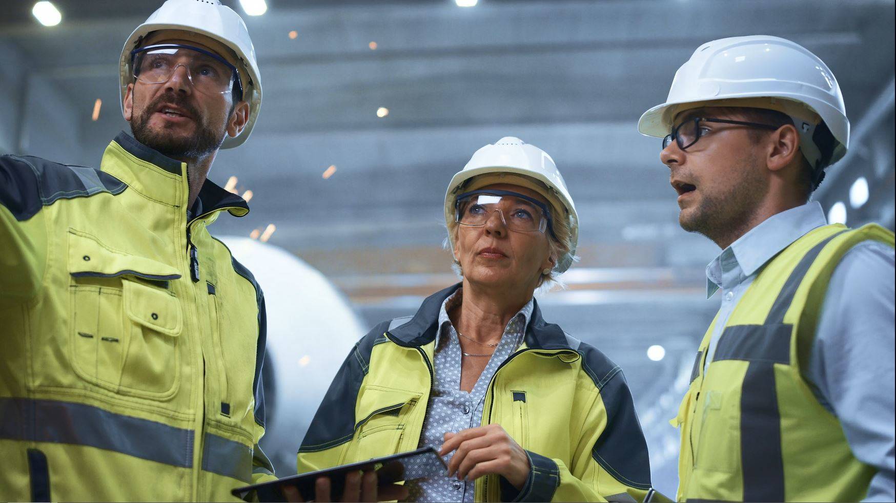 Two men and a woman wearing safety vests, hard hats, and safety glasses. 