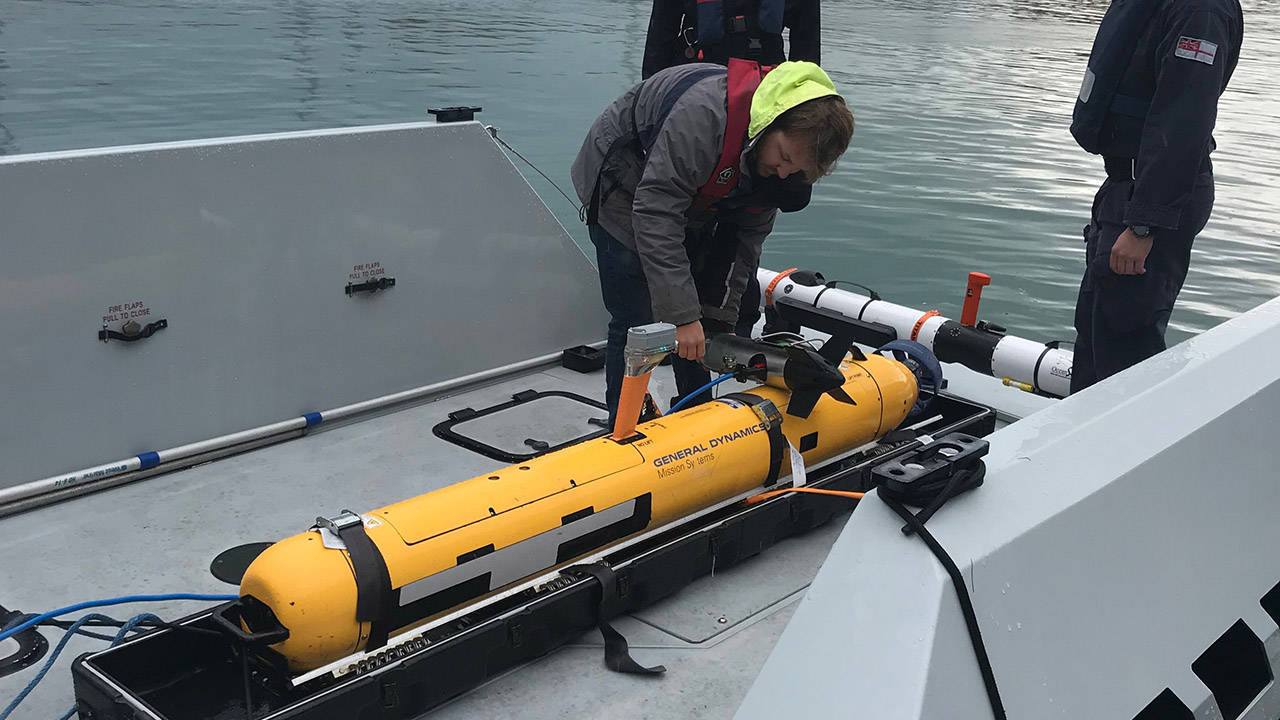 Man hoisting unmanned underwater vehicle into rig on boat