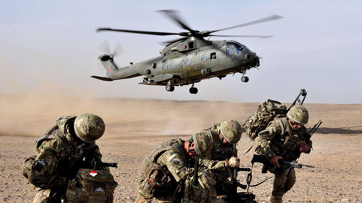 Three soldiers crouching as helicopter lands in background