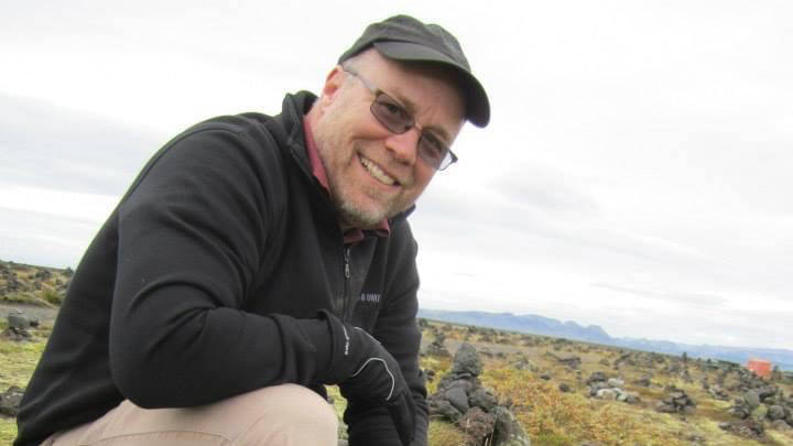 Man with hat kneels on rocky hill