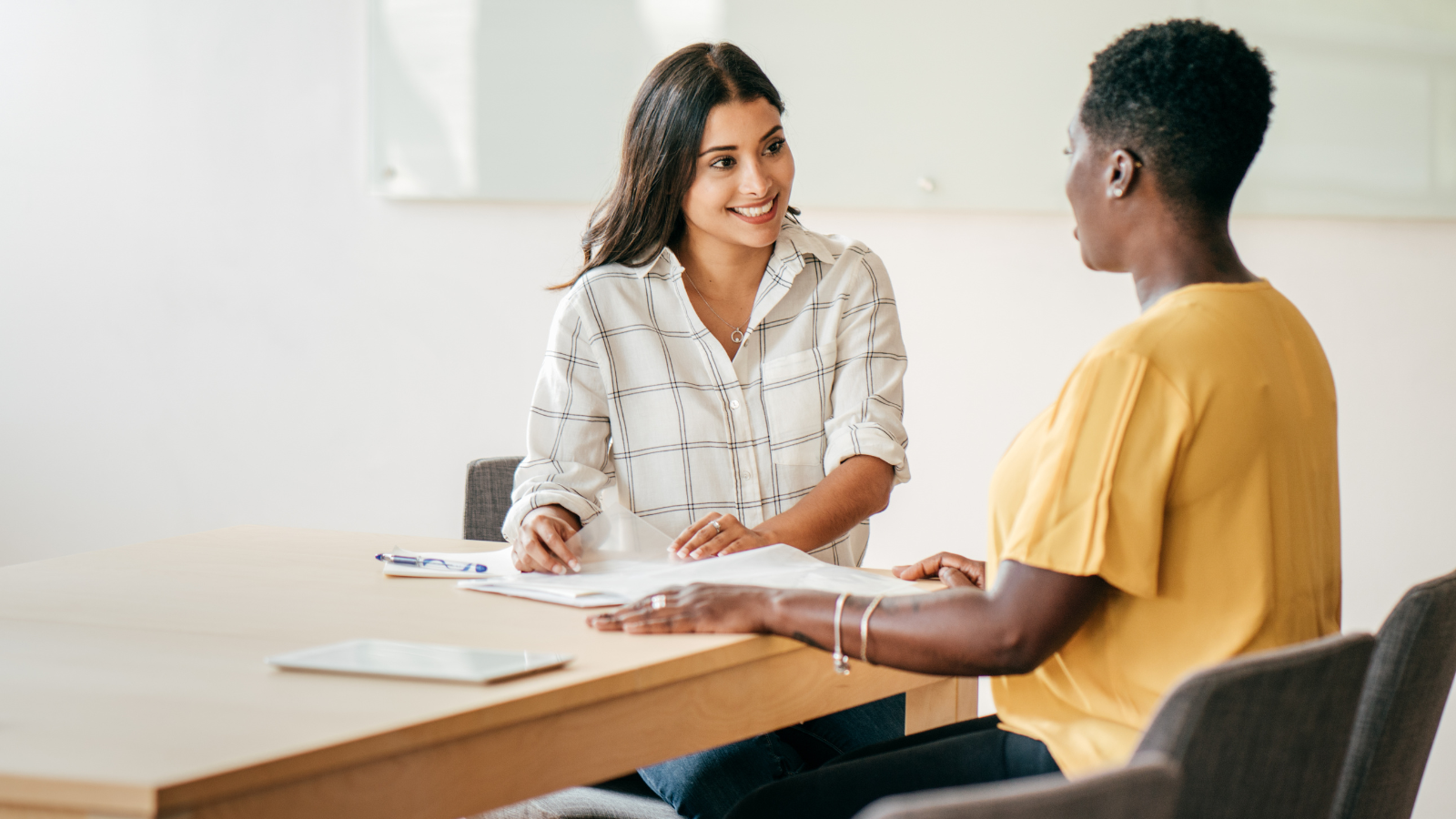 Two woman sitting at a desk chatting.