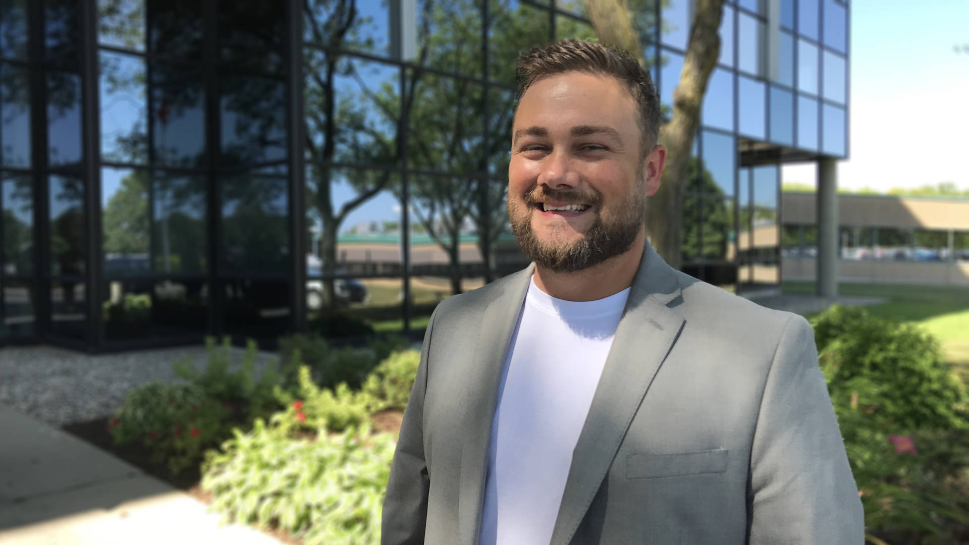 Man smiling at camera in front of office building.
