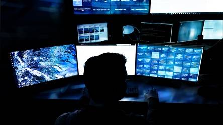 Person in dark room at desk with 3 monitors