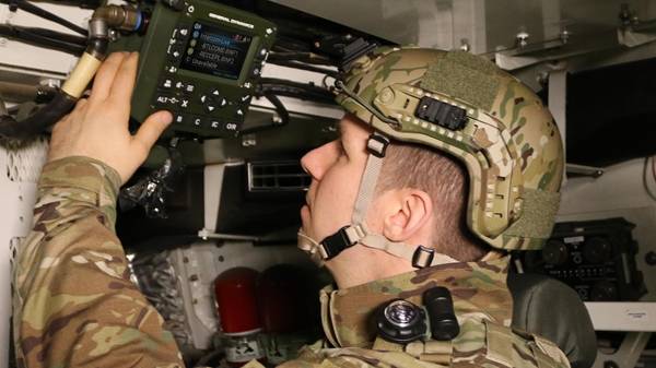 UK soldier with helmet pressing button on intercom box inside military vehicle